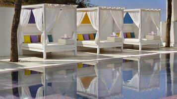 A poolside area with four white canopy beds, each with colorful pillows.
