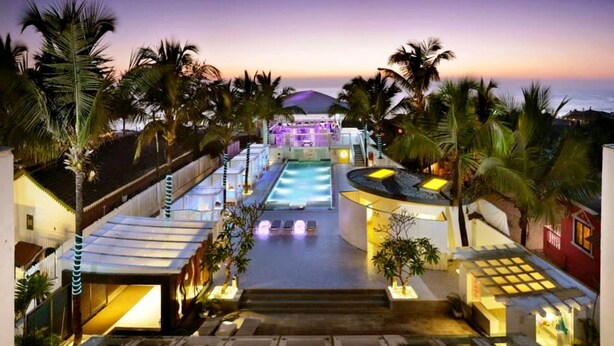 Un resort con piscina, palmeras y vista al océano al atardecer.