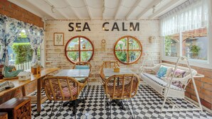 Een gezellig café met een 'SEA CALM' bord, rieten meubels, geruit vloer en een bakstenen muur.