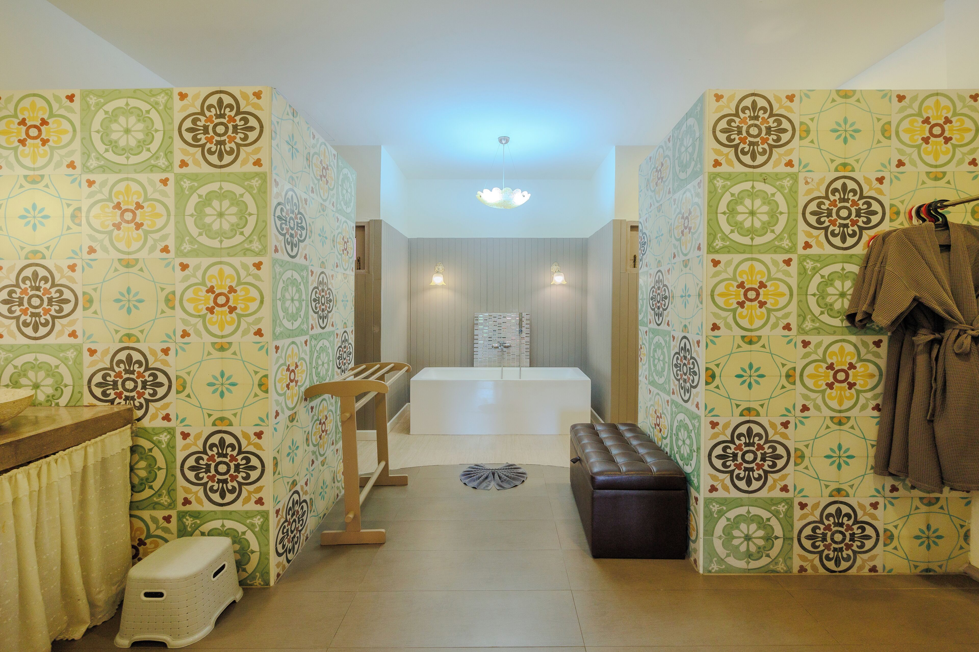 A bathroom with patterned tiles, a bathtub, a bench, and a towel rack.