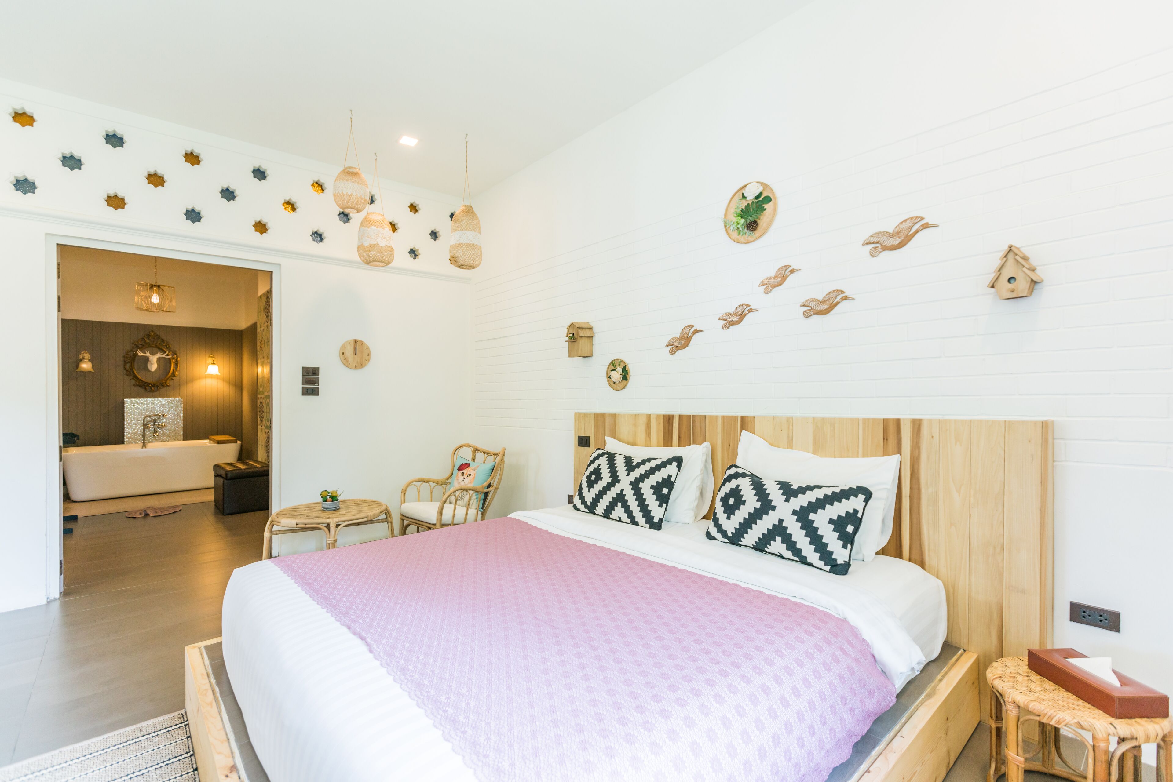 A bedroom with a wooden headboard, a large bed with patterned pillows, a bedside table, and a wall decorated with bird-shaped ornaments.