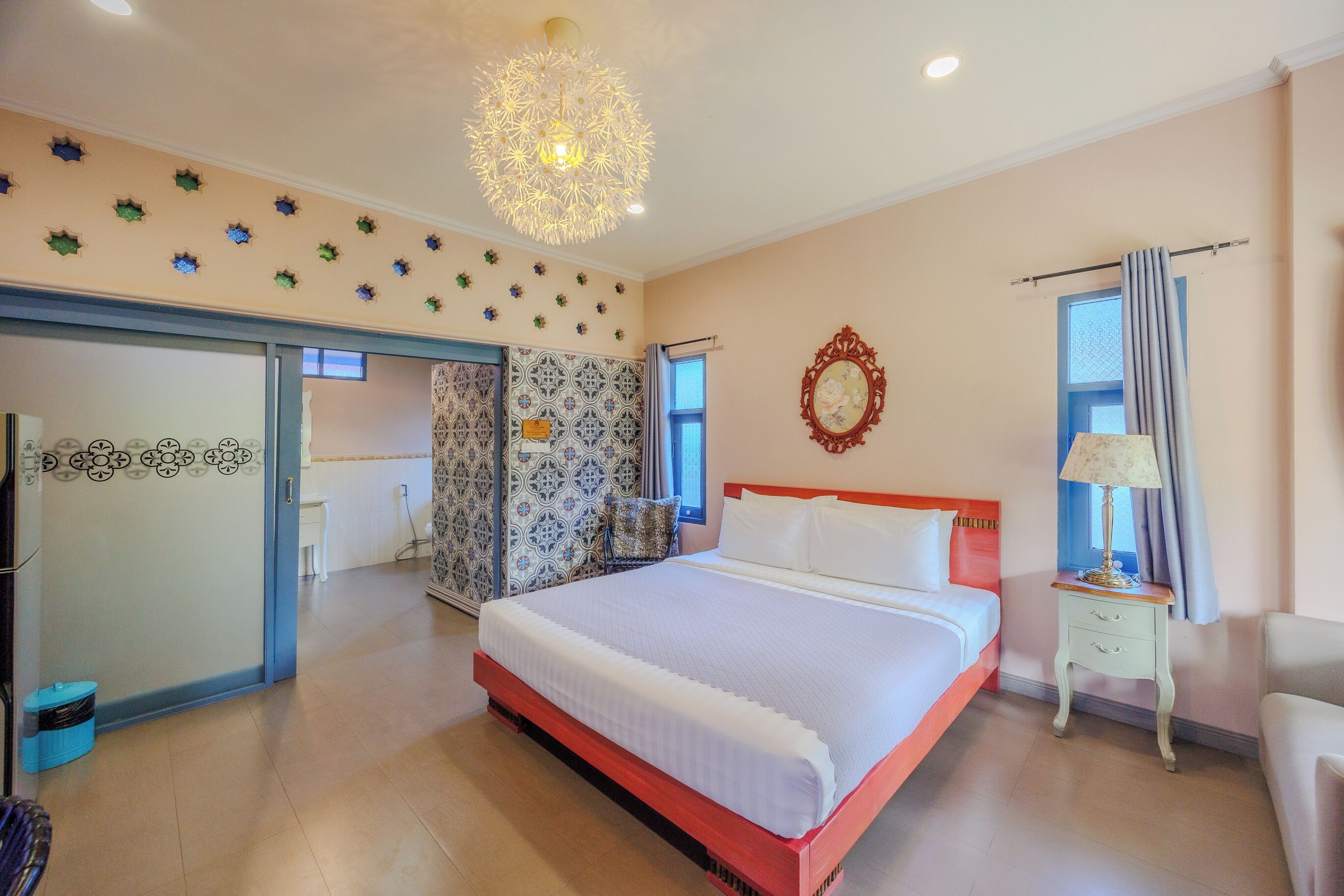 A hotel room with a large bed, a nightstand, a chair, a wardrobe, and a decorative ceiling light.