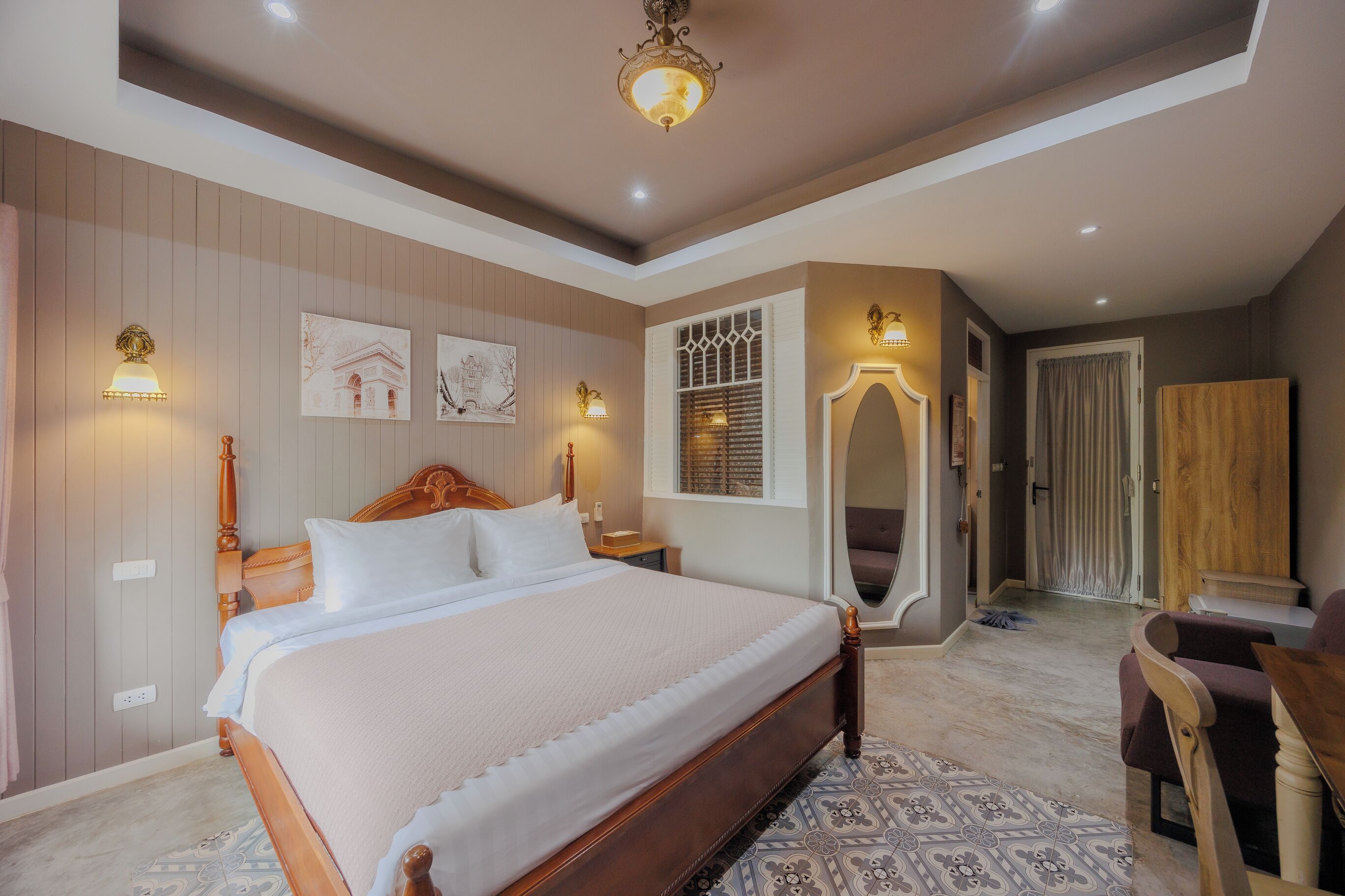 A bedroom with a large bed, a wooden headboard, a patterned rug, and a ceiling light fixture.