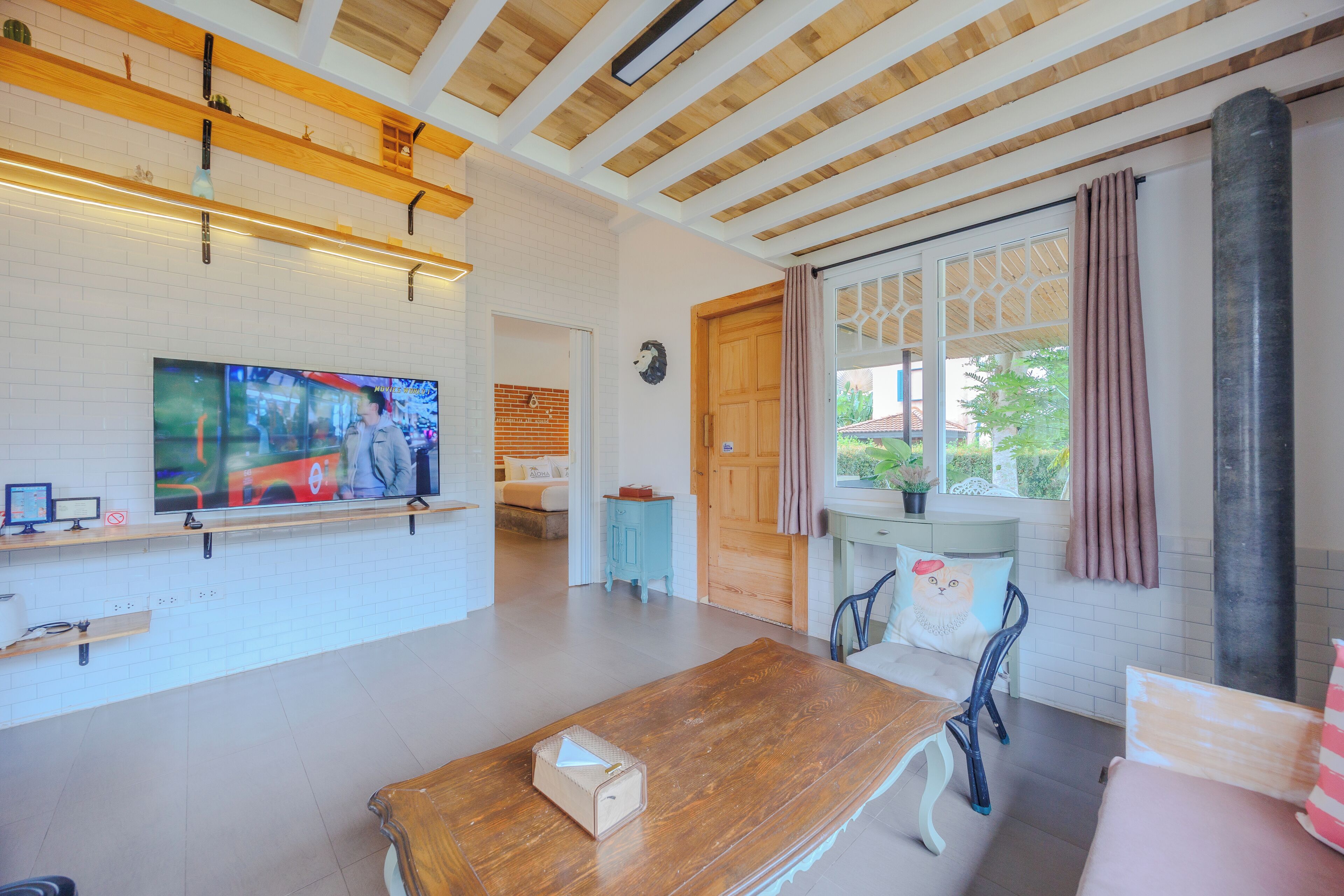 Una habitación amplia con techo de madera, un televisor grande en la pared, una mesa de madera y una ventana con cortinas.