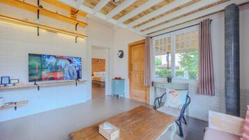 Una habitación amplia con techo de madera, un televisor grande en la pared, una mesa de madera y una ventana con cortinas.