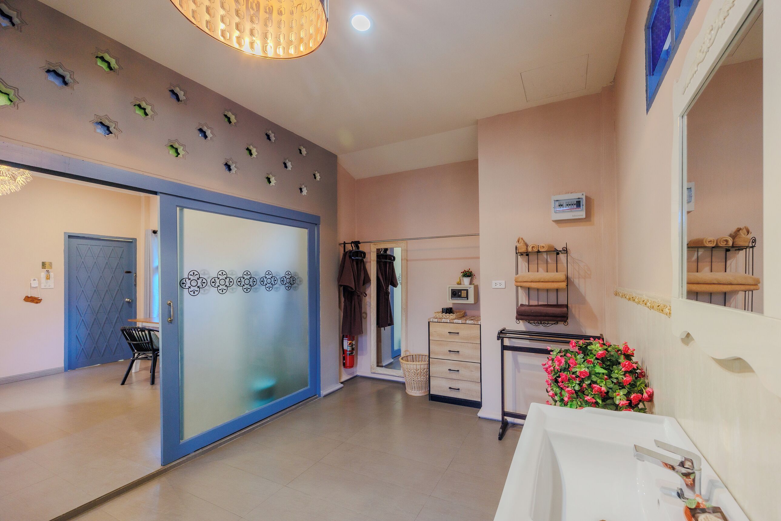 A hotel room with a sliding door, a sink, a mirror, a small plant, and a ceiling light fixture.