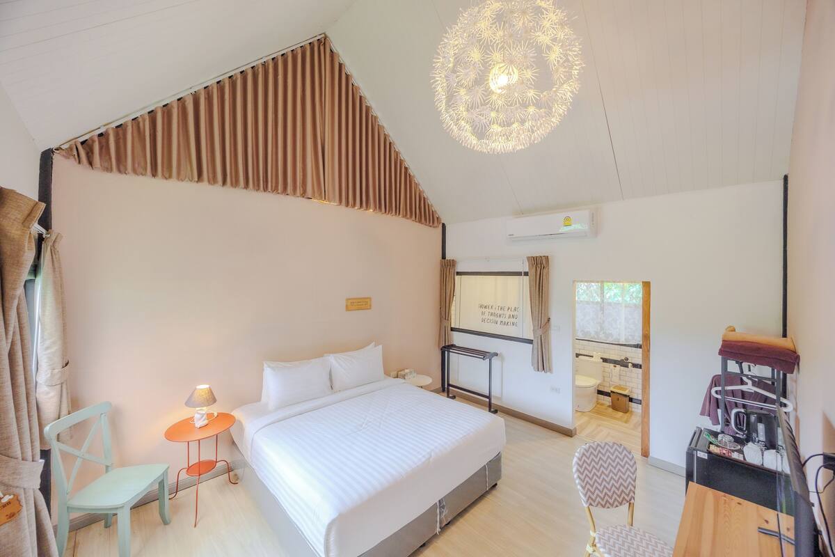 Ein Schlafzimmer mit einem großen Bett, einem kleinen Tisch mit Lampe, einem Sessel und einem Schreibtisch mit Wasserkocher.
