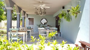Un patio al aire libre con pared de ladrillo, ventilador de techo, plantas colgantes y una mesa con sillas.