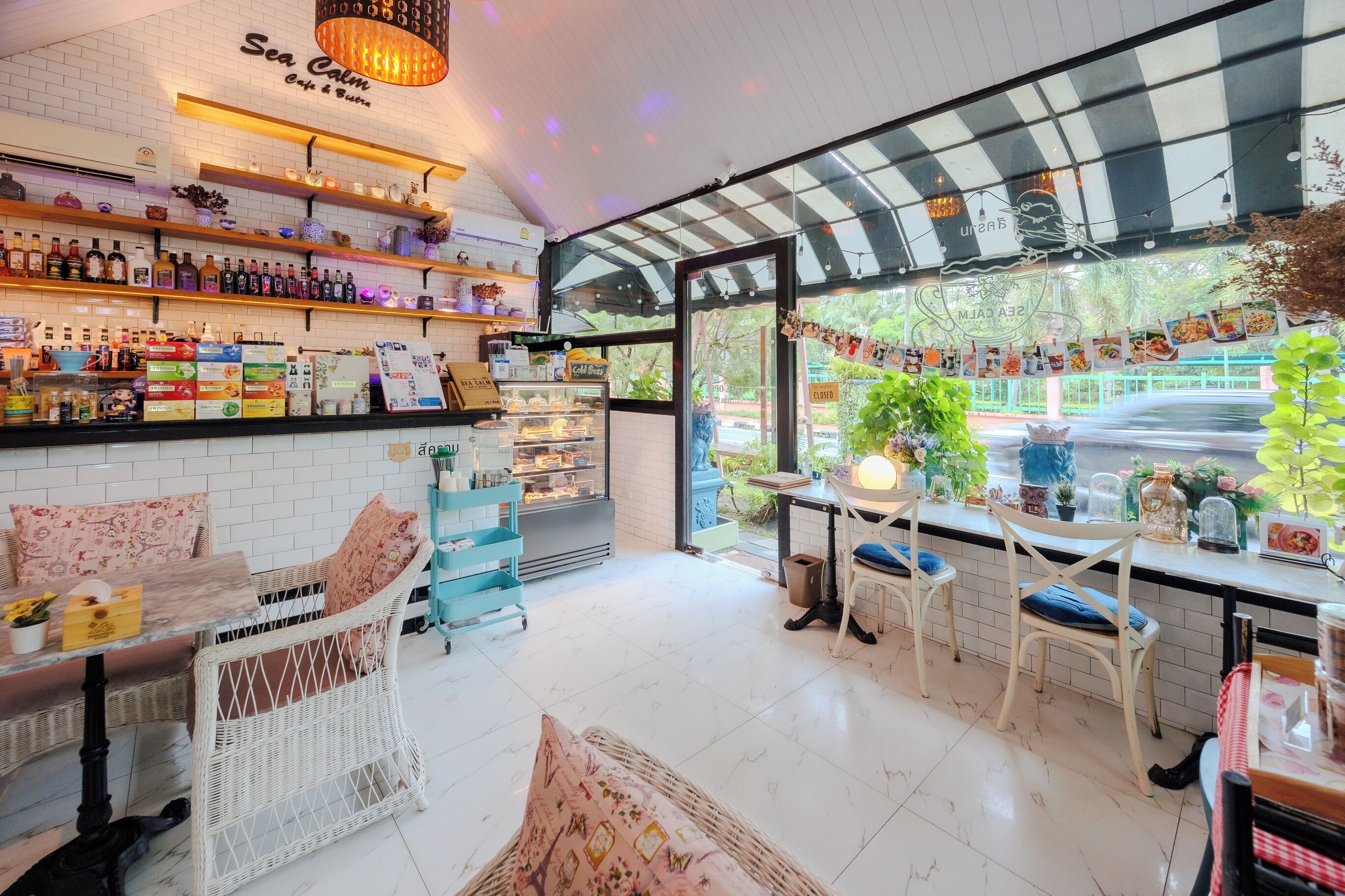 Un café con paredes de azulejos blancos, mobiliario de mimbre y una variedad de bebidas en estantes.