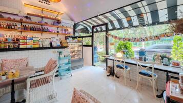 Un café con paredes de azulejos blancos, mobiliario de mimbre y una variedad de bebidas en estantes.