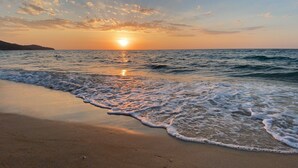 Een strand bij zonsondergang, met golven die zachtjes op het strand komen rollen.