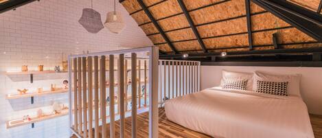 A bedroom with a sloped ceiling, wooden flooring, a bed with white bedding, and a white wall with shelves displaying various items.