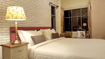 A neatly made bed with white linens, a wooden nightstand with a lamp, and a window with curtains.