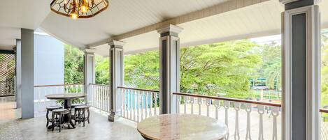 A covered outdoor area with a round table and four chairs, columns, and a railing with a view of greenery.