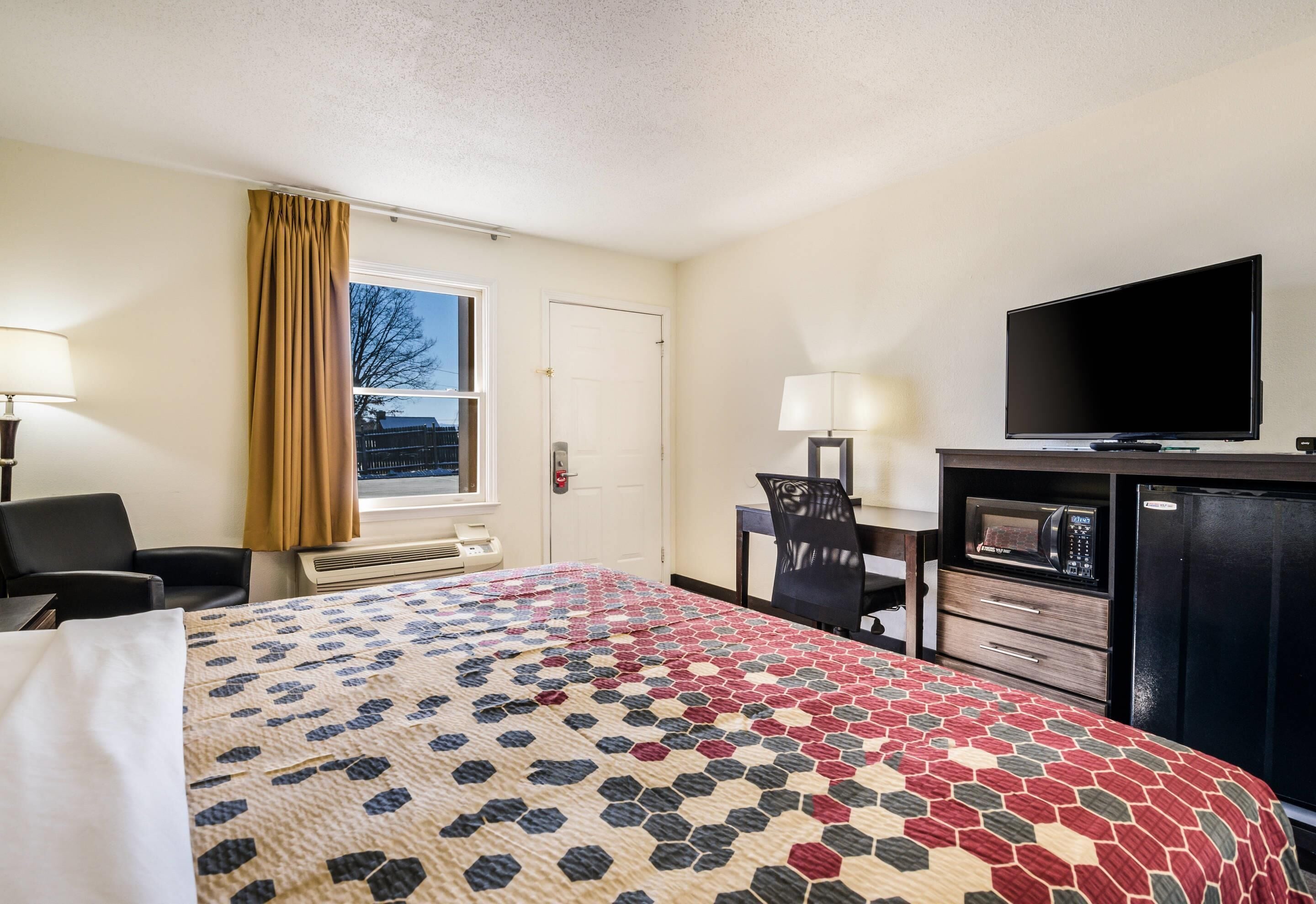 A hotel room with a bed, a desk, a chair, a television, a microwave, and a refrigerator.