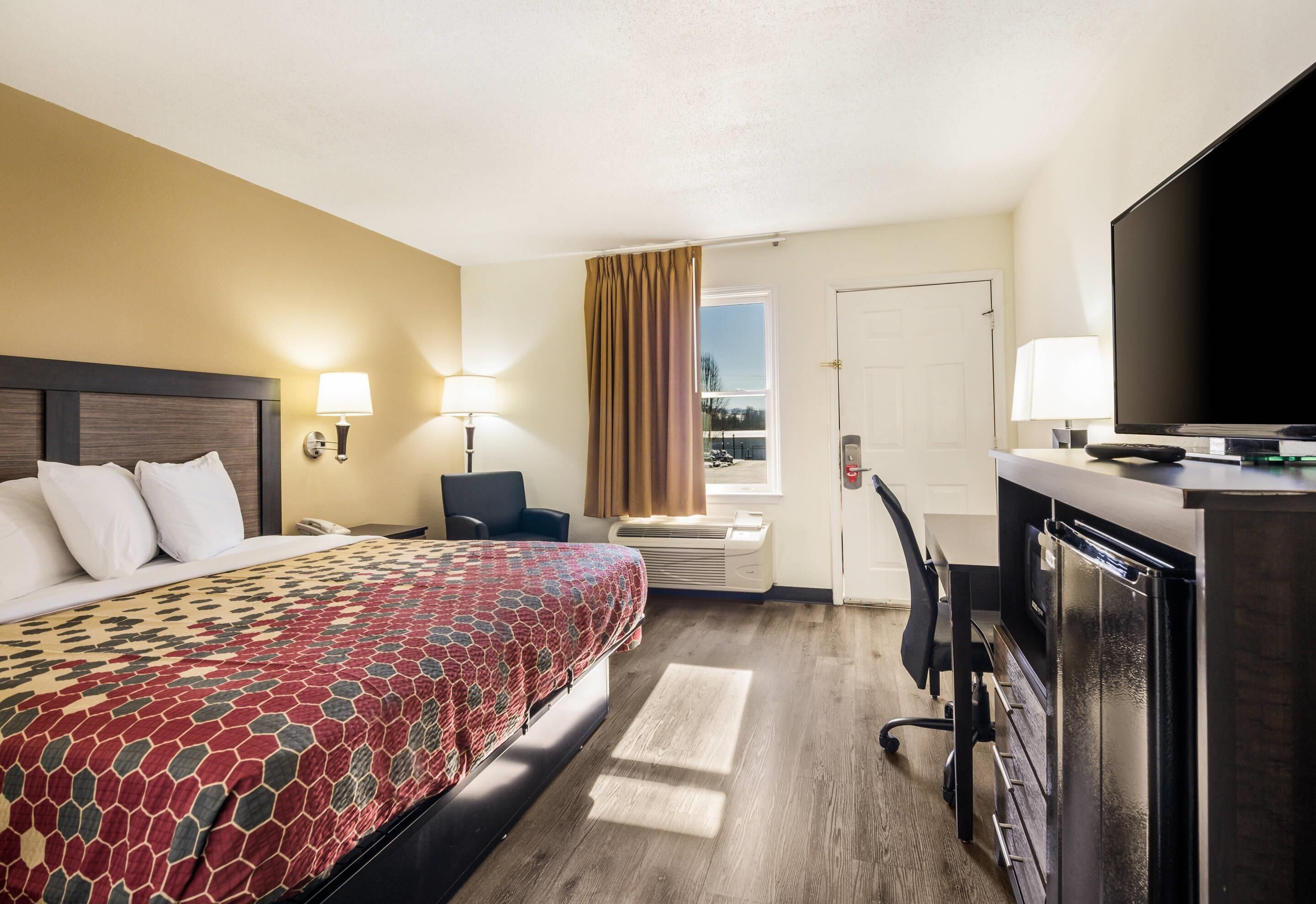 A hotel room with a bed, desk, TV, and a view of the outdoors.