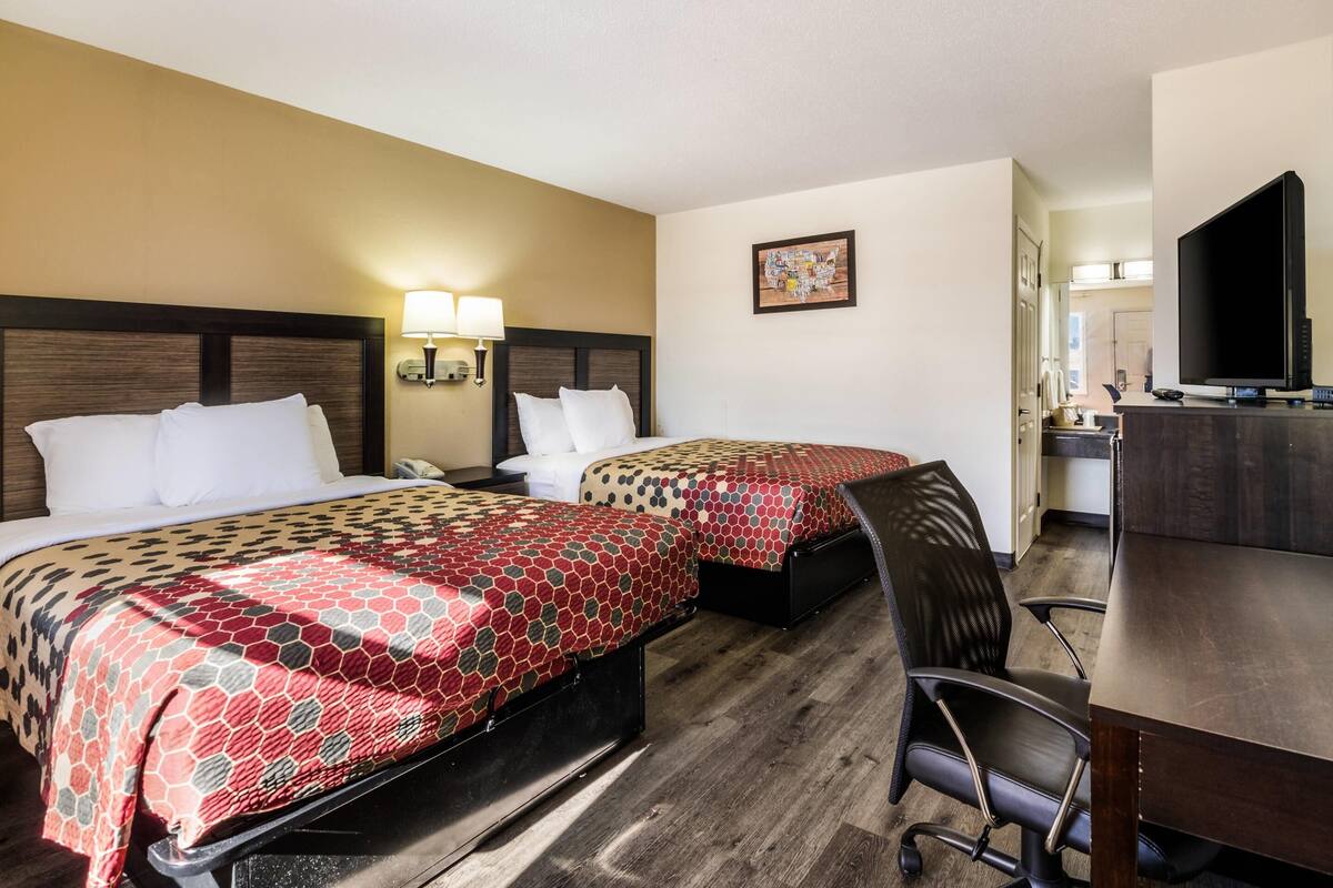 A hotel room with two beds, a desk, a chair, a TV, and a bathroom visible in the background.