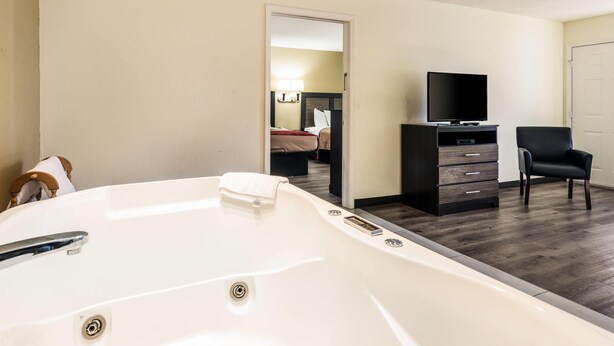 Una habitación de hotel con una bañera blanca grande, un televisor en una cómoda y una silla.