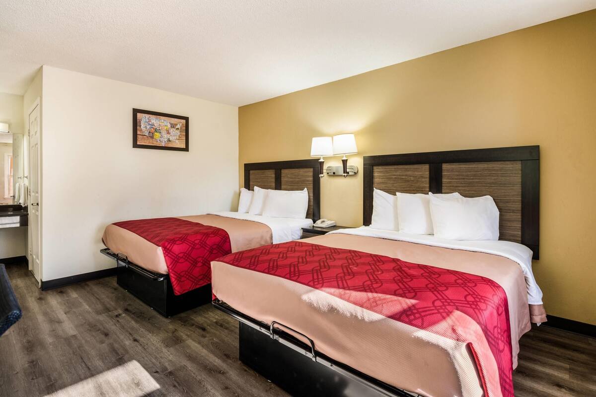 A hotel room with two beds, each with a red and beige bedspread, a wooden headboard, bedside lamps, and a small table with a phone.