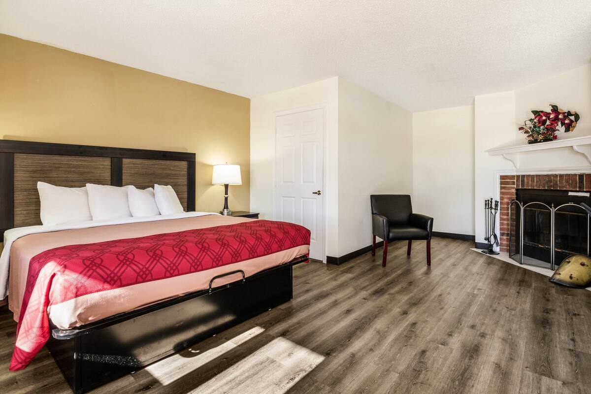 A hotel room with a bed, a chair, a fireplace, and a door.