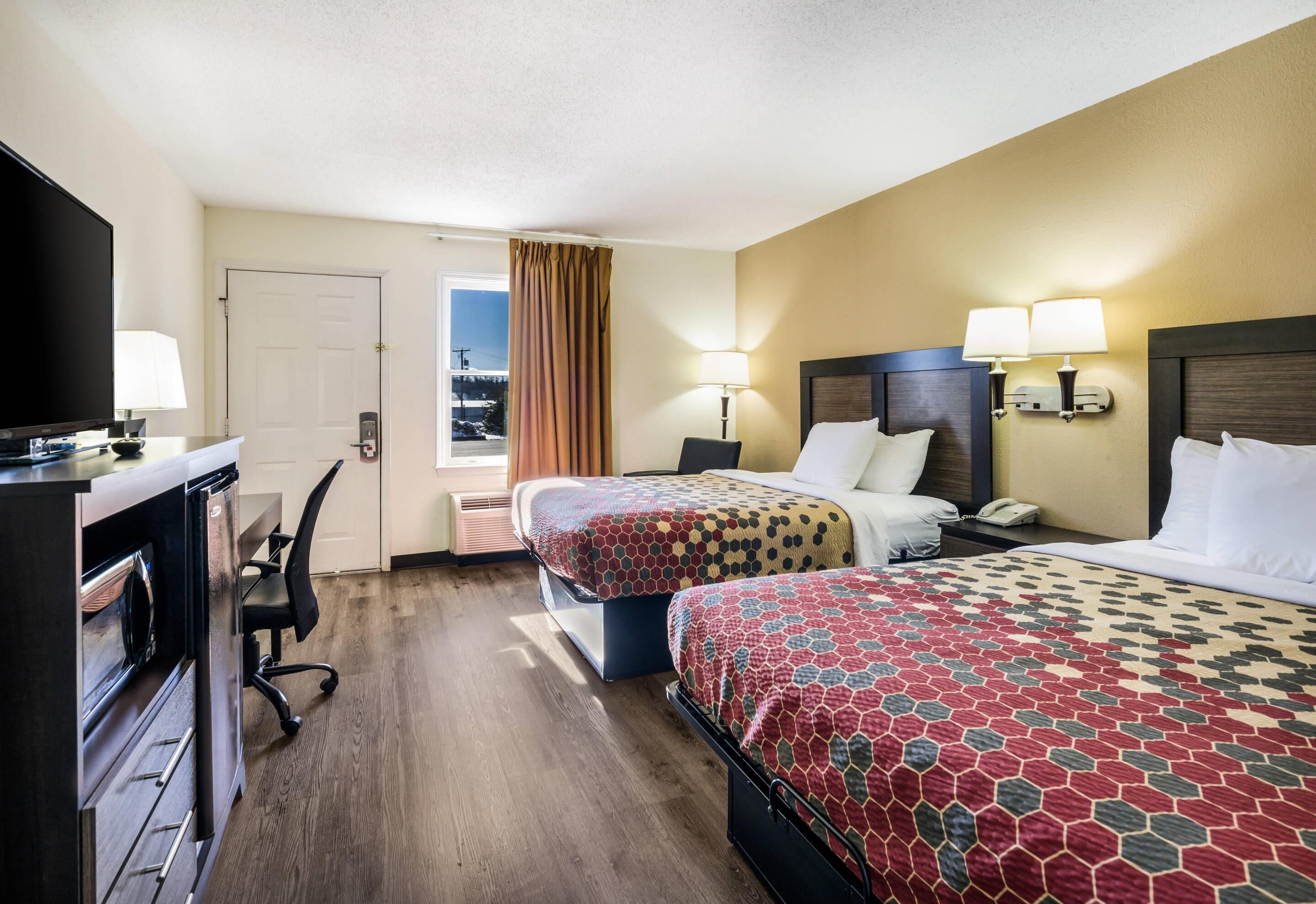 A hotel room with two beds, a desk with a computer, a TV, and a window with curtains.