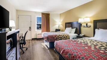 Quarto de hotel com duas camas, uma escrivaninha com computador, televisão e janela com cortinas.