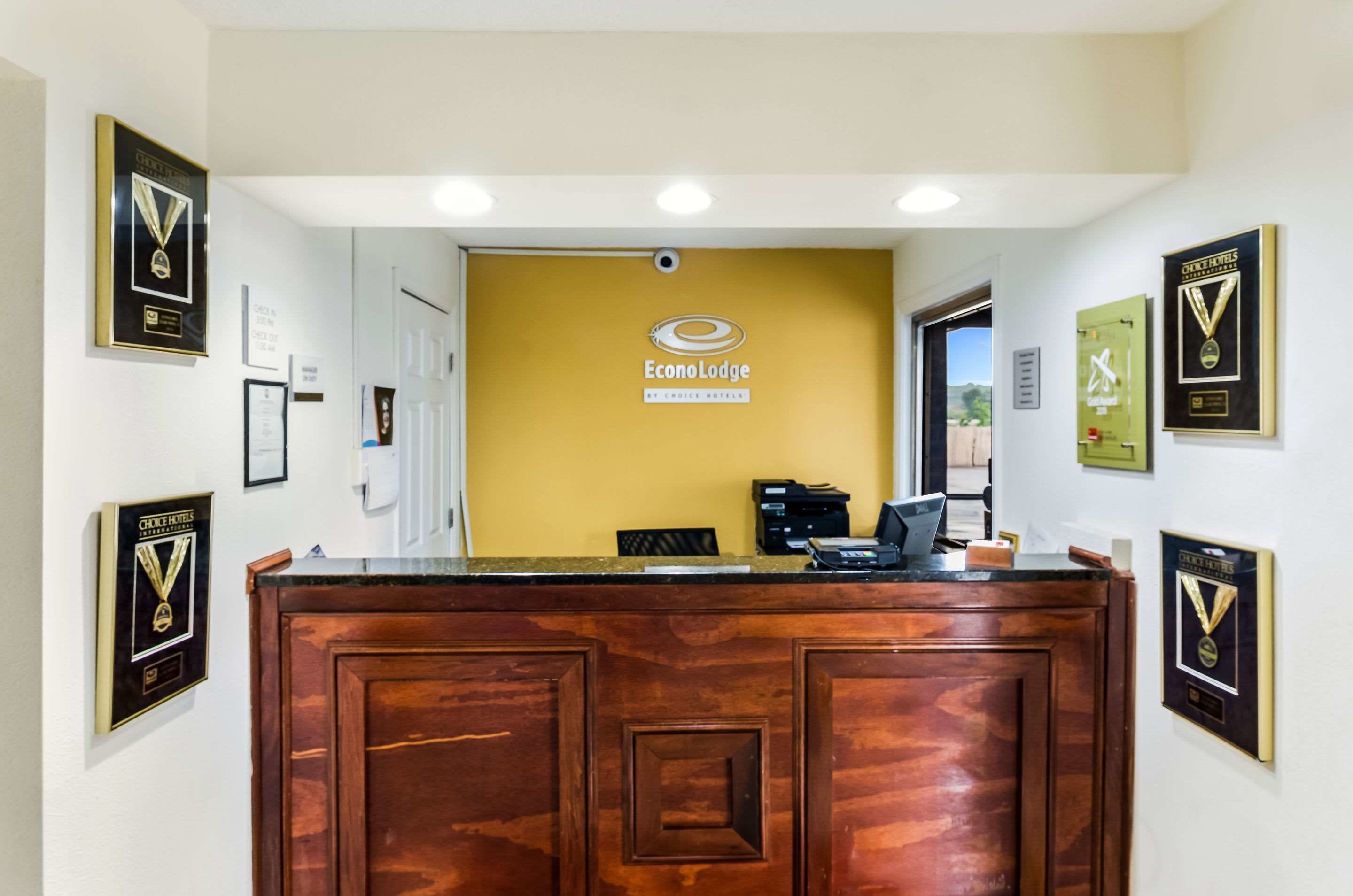 Un mostrador de recepción con detalles de madera, un letrero que dice "Econo Lodge by Choice Hotels" y varios premios enmarcados en las paredes.