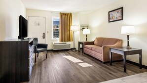 Habitación de hotel con escritorio, televisor, sofá, lámpara y ventana con cortinas.