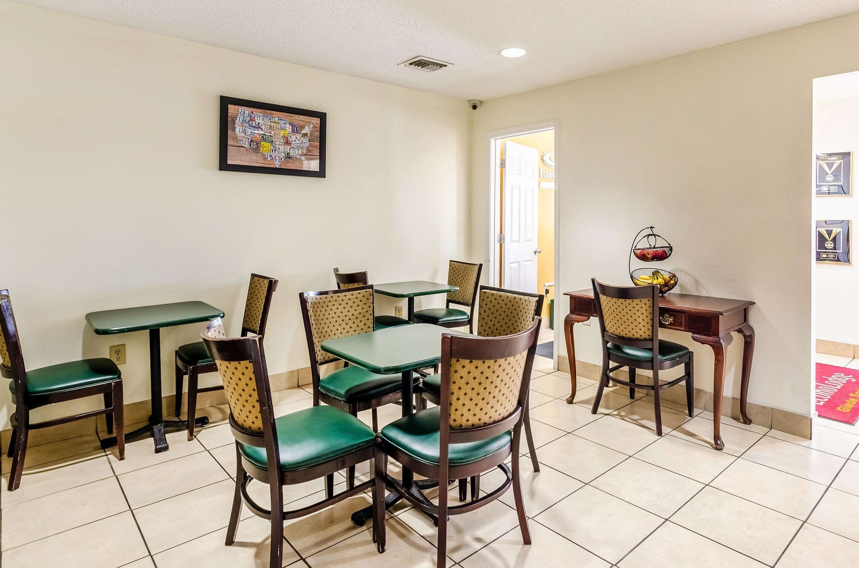 A dining area with multiple tables and chairs, a framed picture on the wall, and a door leading to another room.