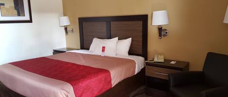 A hotel room with a large bed, two bedside tables, a desk with a phone, and a chair.