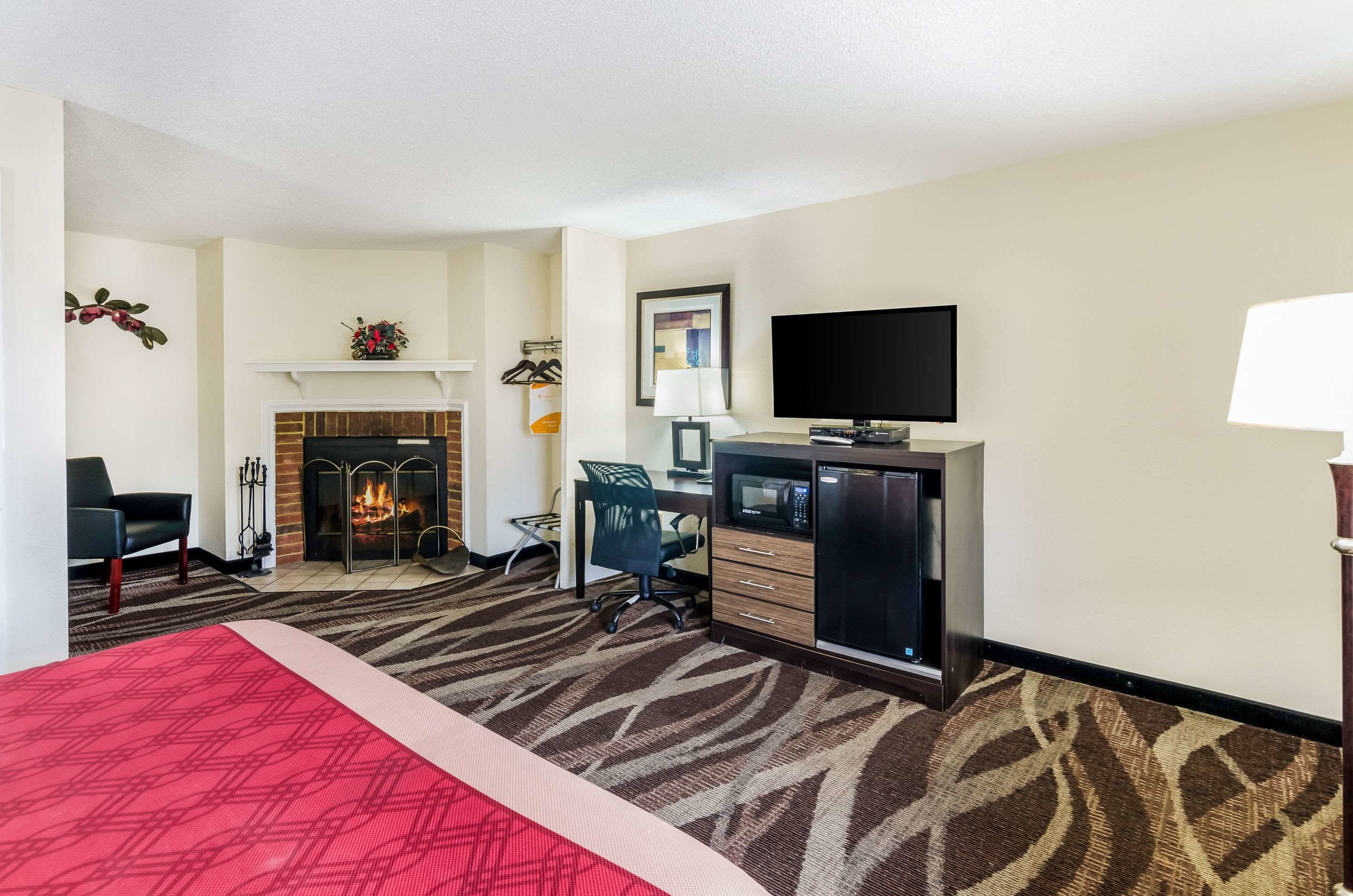 A hotel room with a bed, a desk, a television, a fireplace, and a carpeted floor.