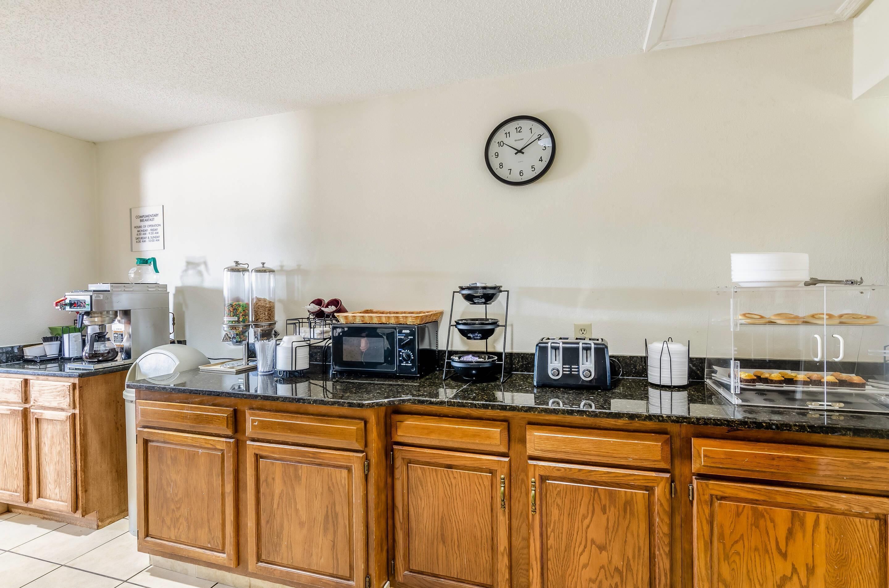 A kitchen with wooden cabinets, a microwave, toaster, and a clock on the wall.