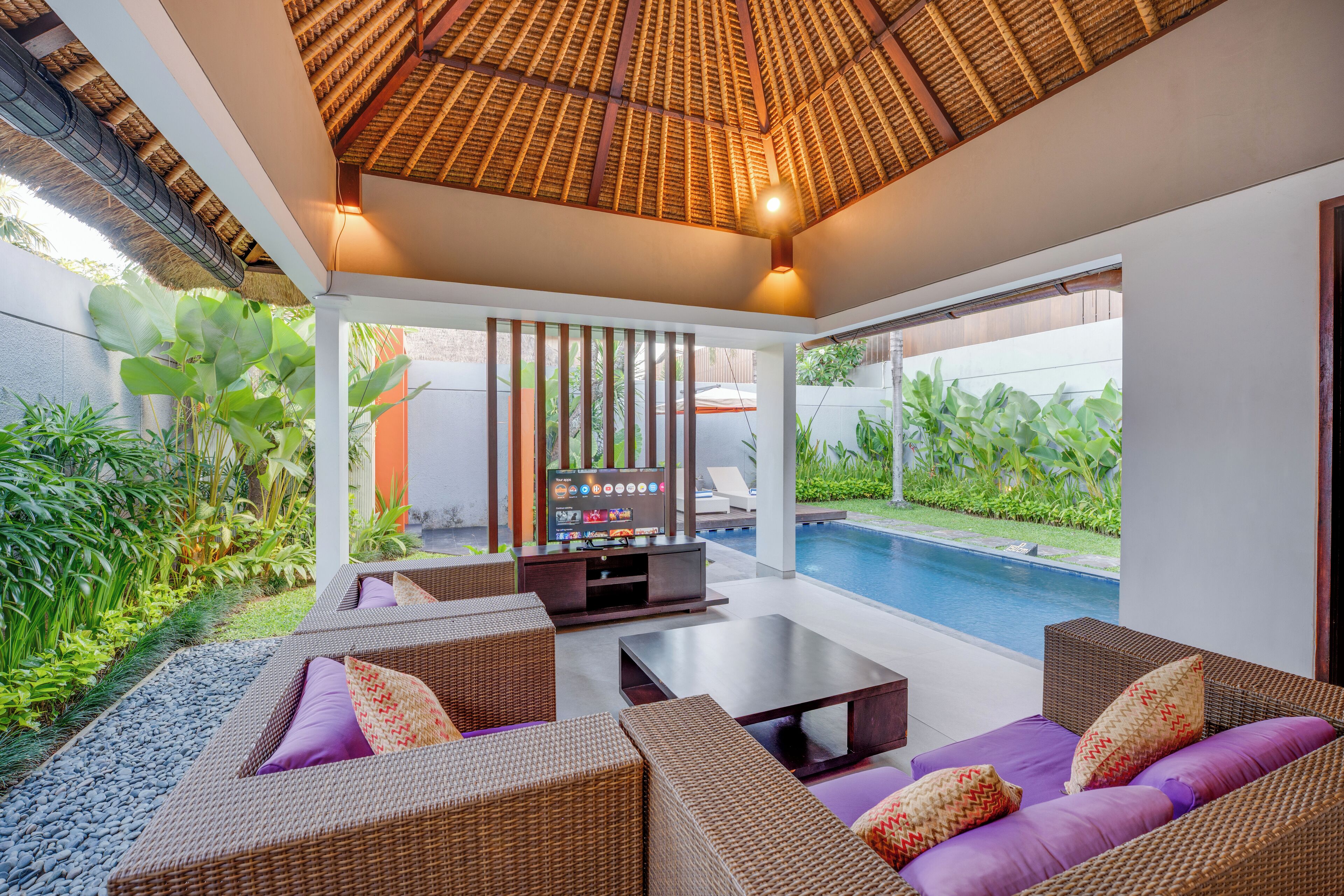 A modern outdoor living area with wicker furniture, a TV, and a pool.