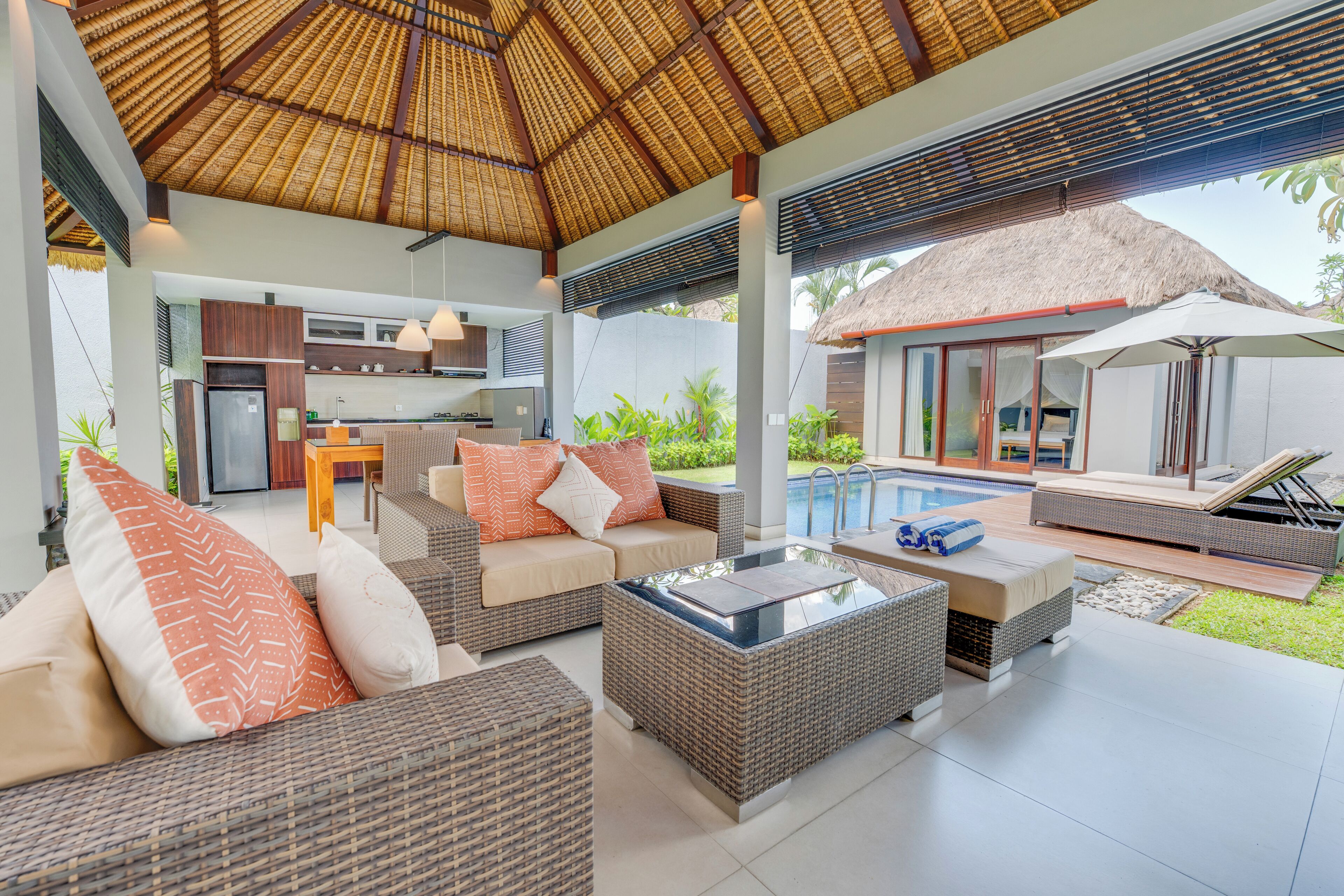 Un espace de vie extérieur moderne, avec des meubles en osier, une table basse en verre et une piscine en arrière-plan.