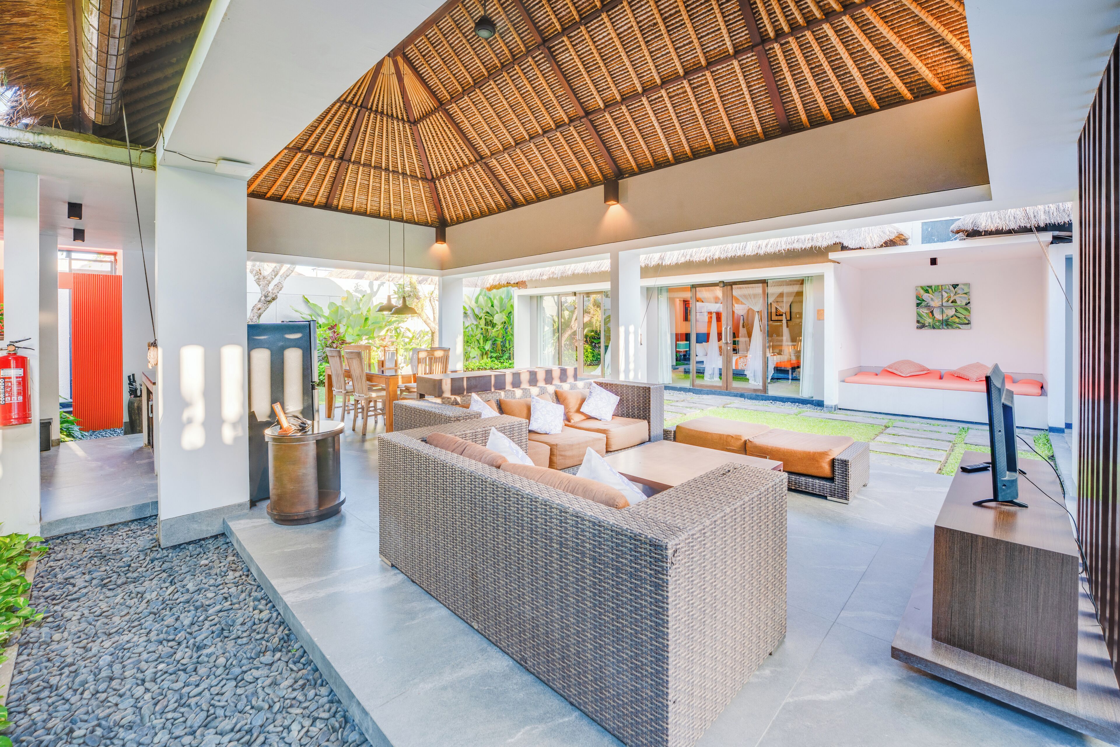 A spacious indoor area with a high ceiling, a large wicker sofa, and a flat-screen TV on a wooden stand.