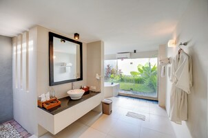 A modern bathroom with a large mirror, white sink, and a view of a garden through the window.