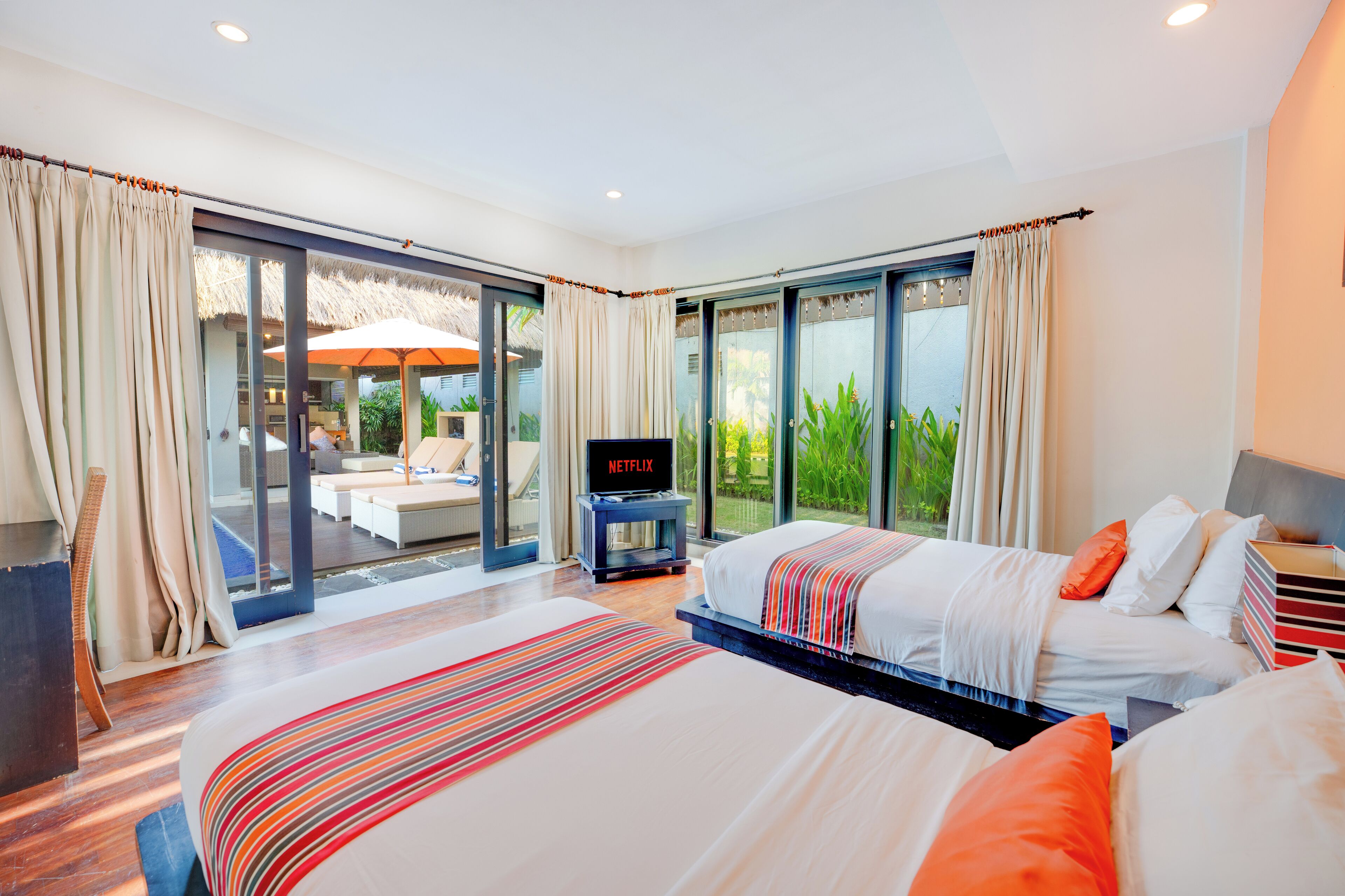 A modern hotel room with two beds, a TV, and a sliding glass door leading to a balcony.