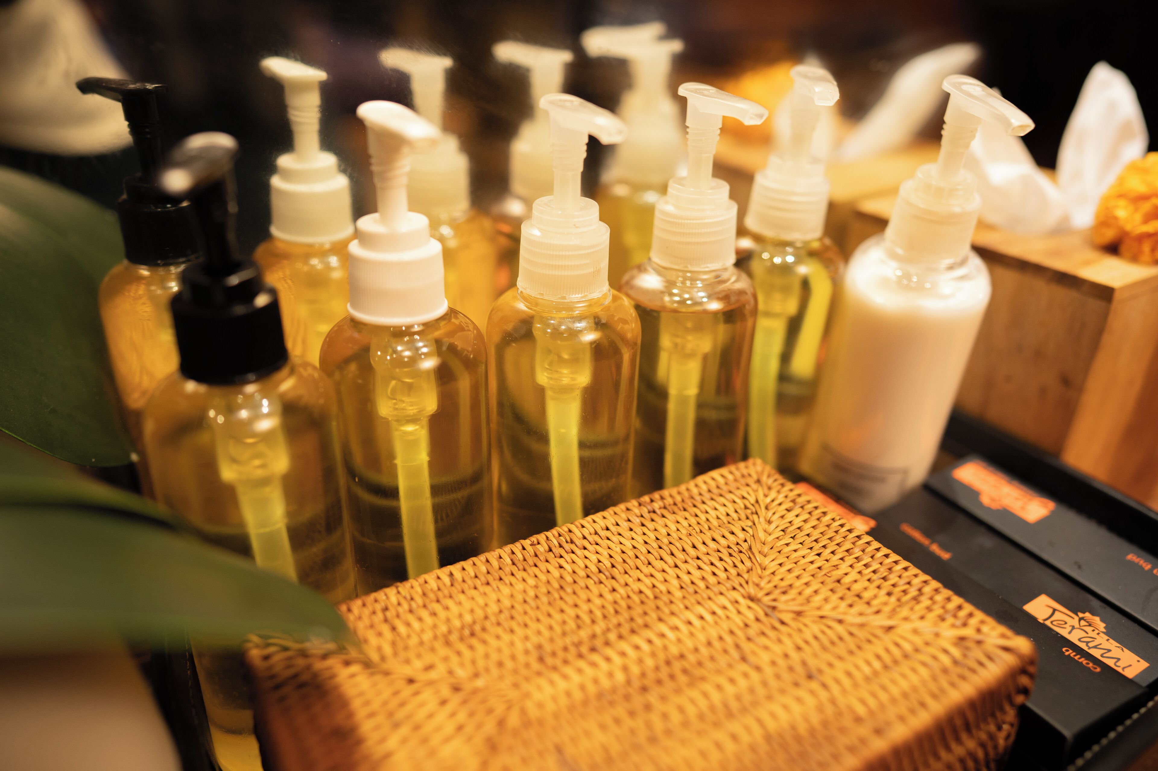 A display of various toiletries including bottles of liquid soap and lotion, arranged on a wooden surface with a woven basket in the foreground.
