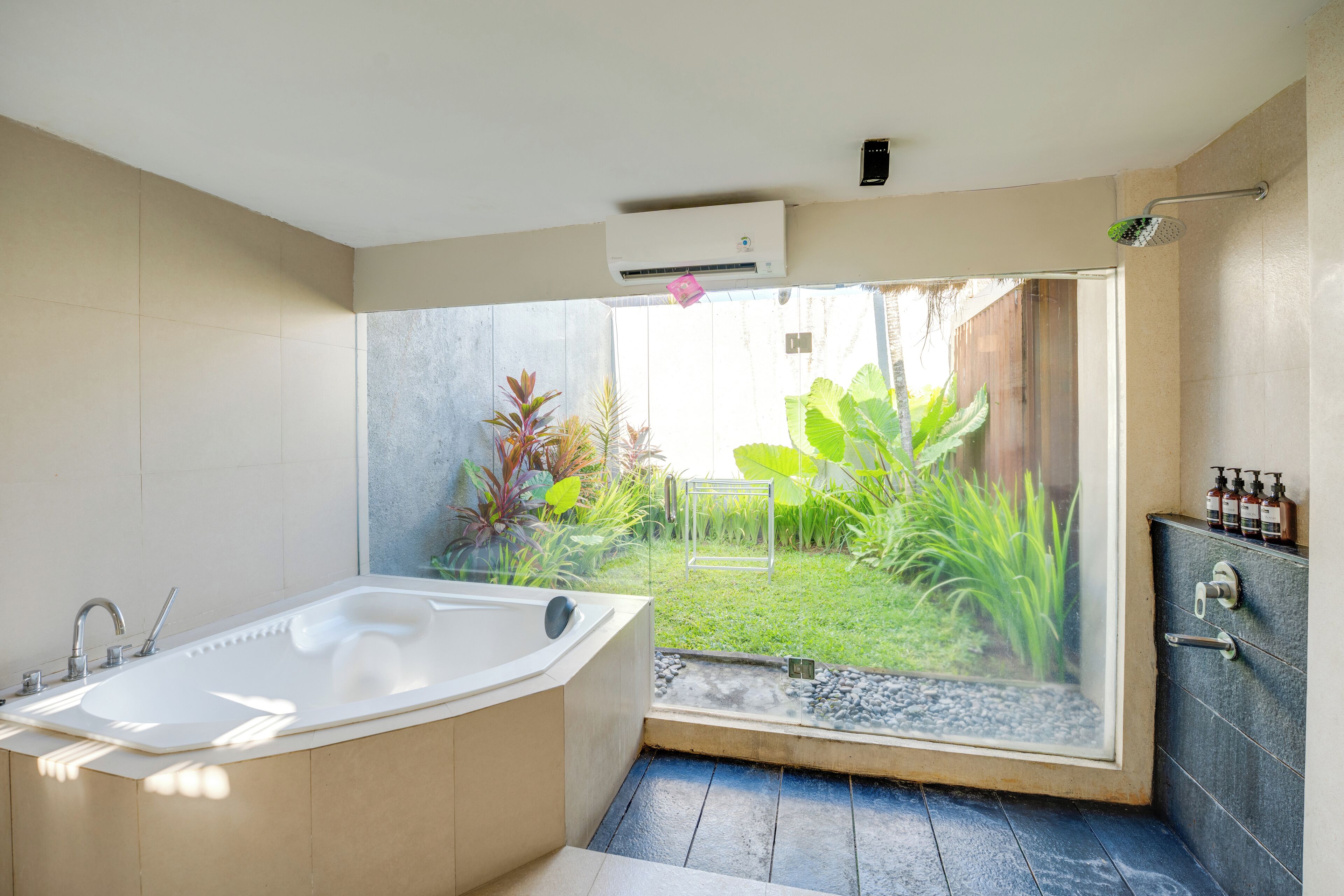 A modern bathroom with a large bathtub, a shower, and a view of a garden through a glass door.
