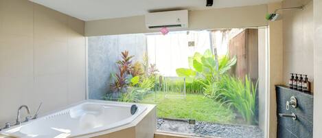 A modern bathroom with a large bathtub, a shower, and a view of a garden through a glass door.