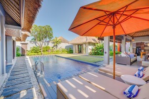 A poolside area with lounge chairs, an umbrella, and a thatched-roof structure.