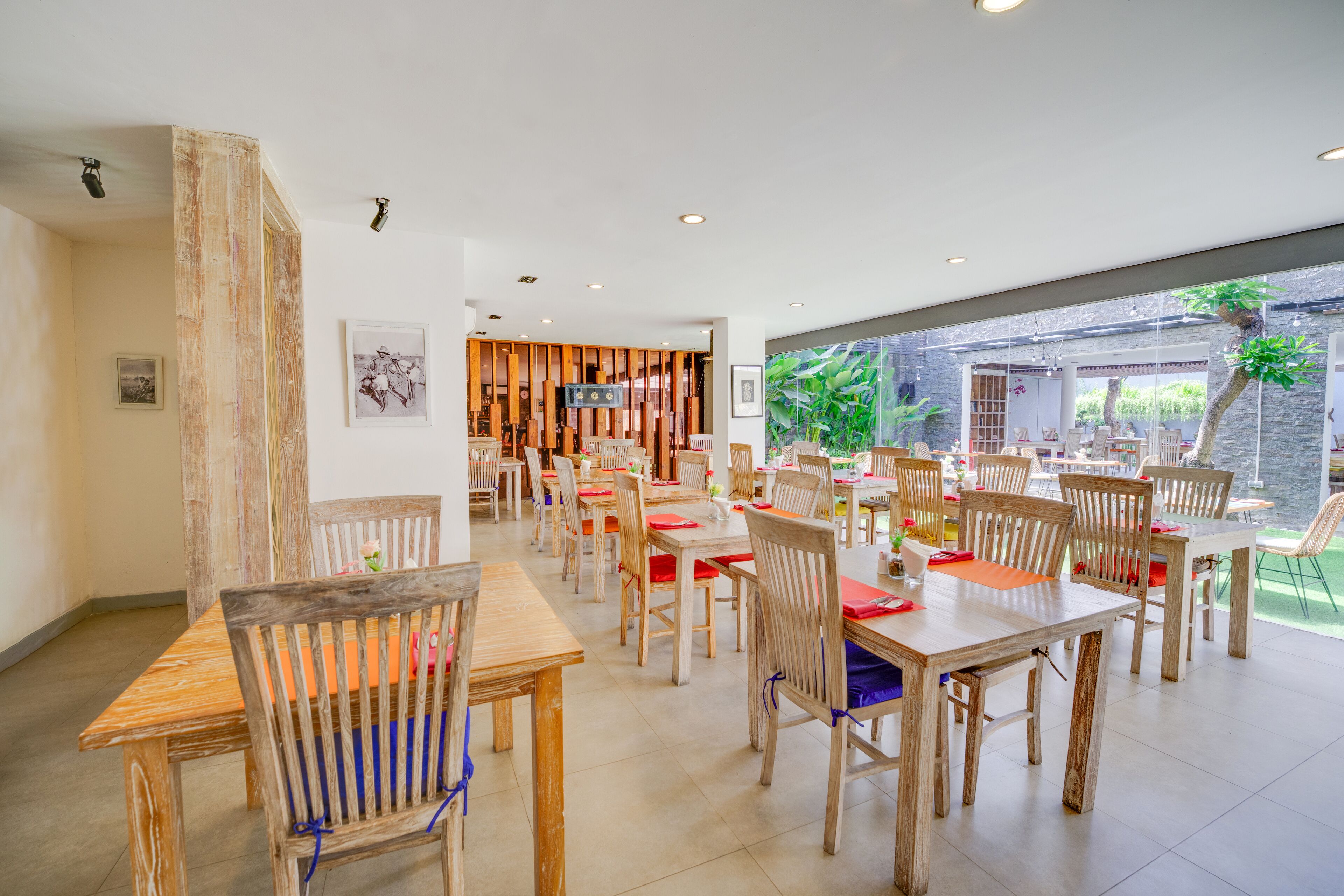 A spacious dining area with wooden tables and chairs, a television, and a view of greenery outside.