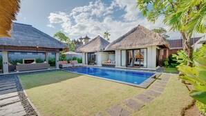 A pool area with thatched-roof structures, a clear sky, and a well-maintained lawn. - Villa Jerami & Spa (Seminyak)
