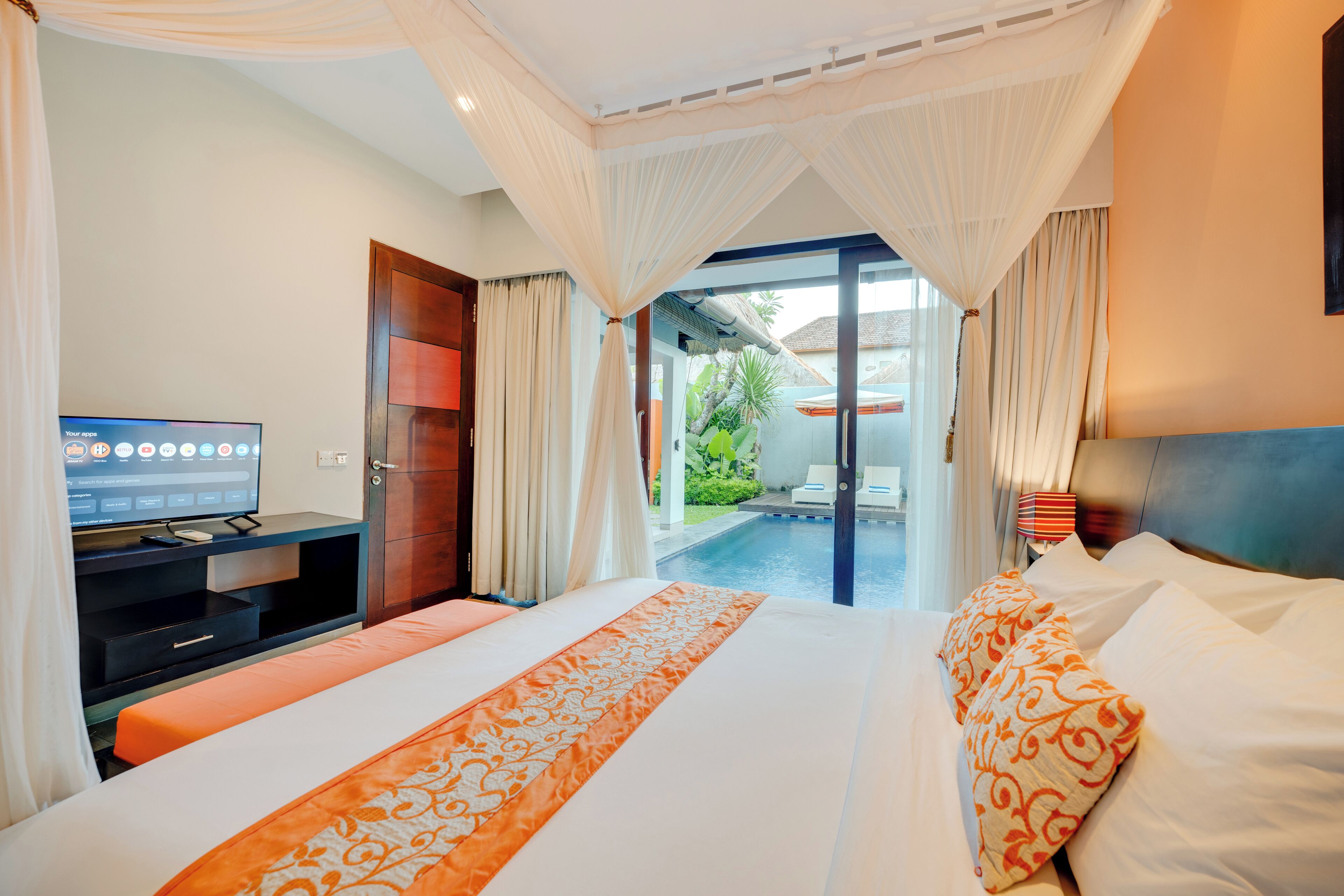 Habitación de hotel con cama, televisor, escritorio y vistas a una piscina y jardín.