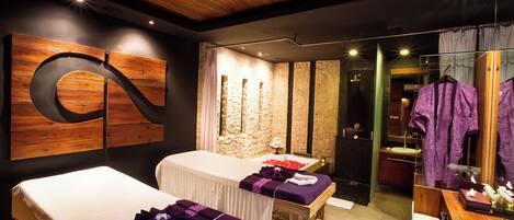 Un cuarto de spa con dos camillas de masaje, una pared de piedra, techo de madera y un espejo con bata.