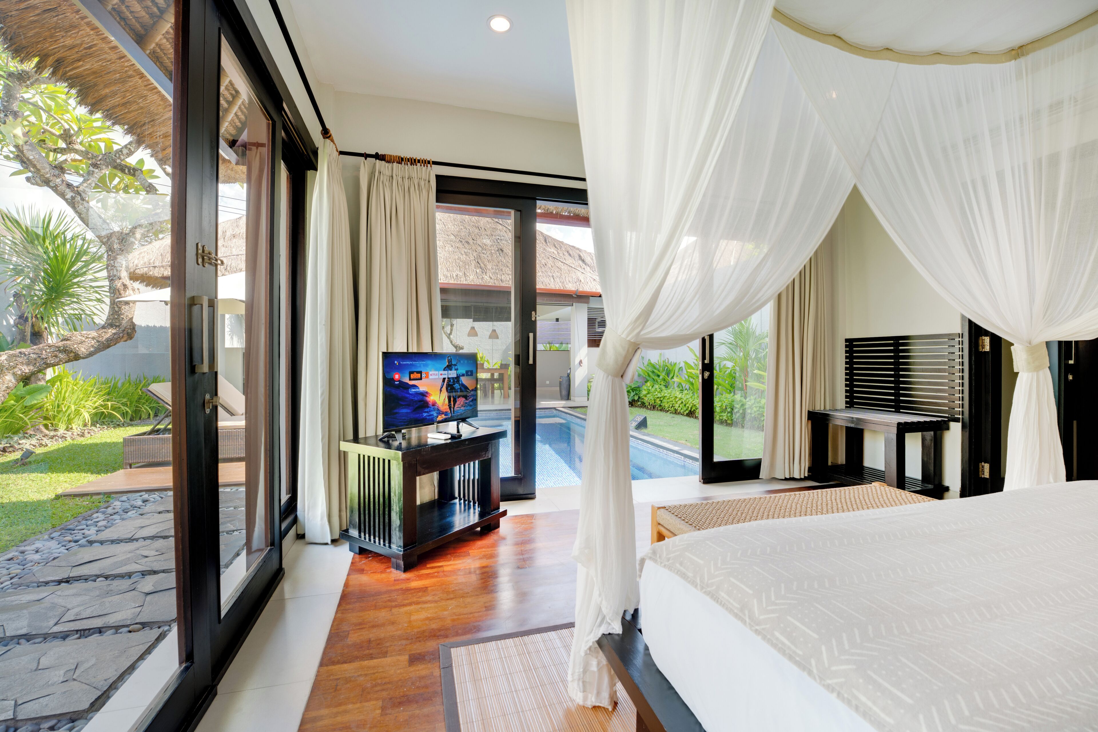 A bedroom with a large bed, a television, and a view of a swimming pool.
