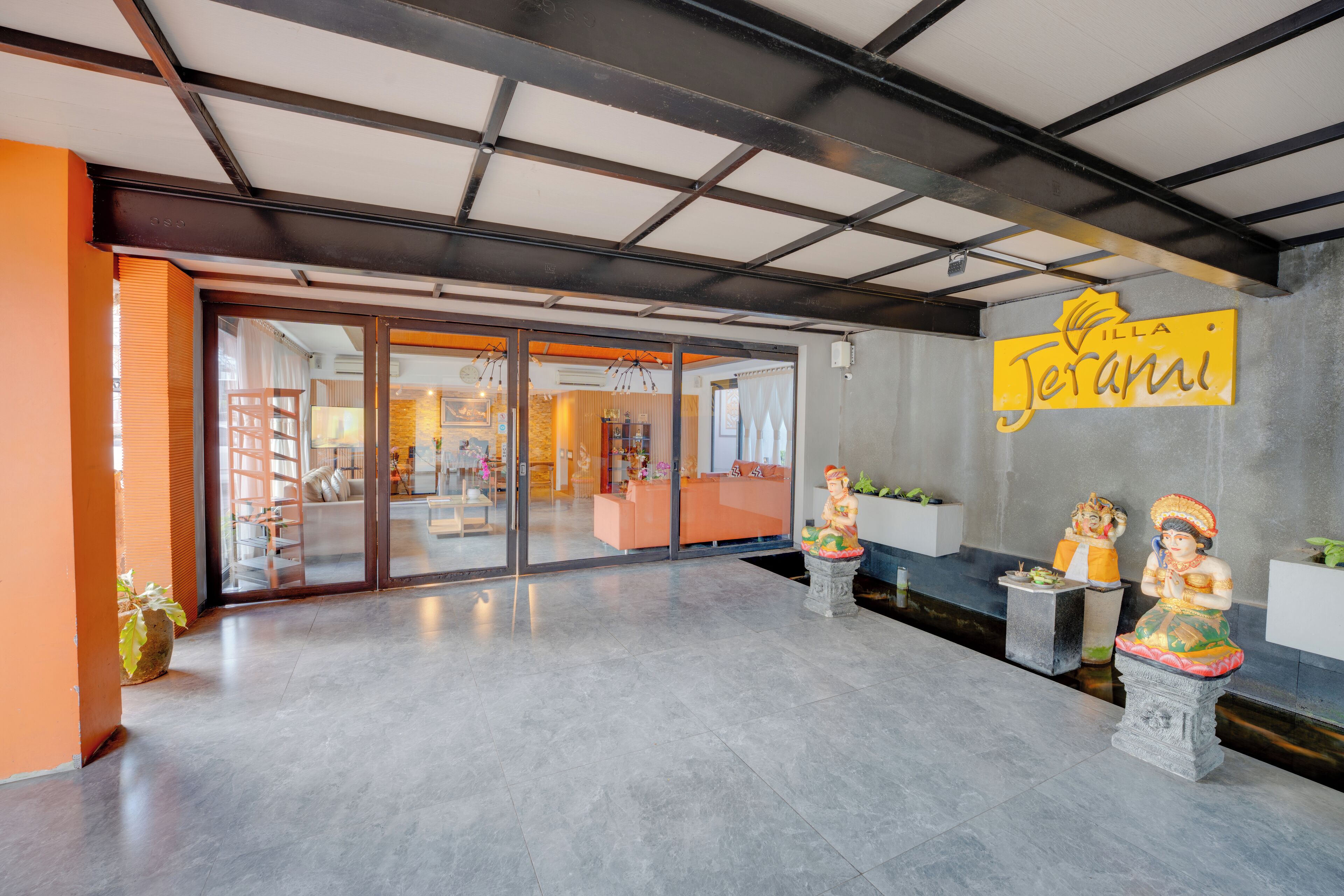 A reception area with a modern design, featuring a glass door entrance, a reception desk, and two statues on pedestals.