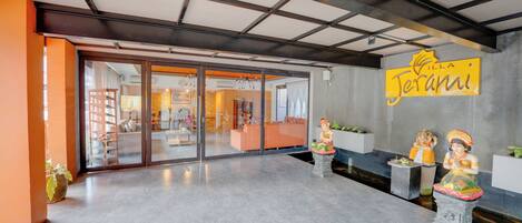 A reception area with a modern design, featuring a glass door entrance, a reception desk, and two statues on pedestals.