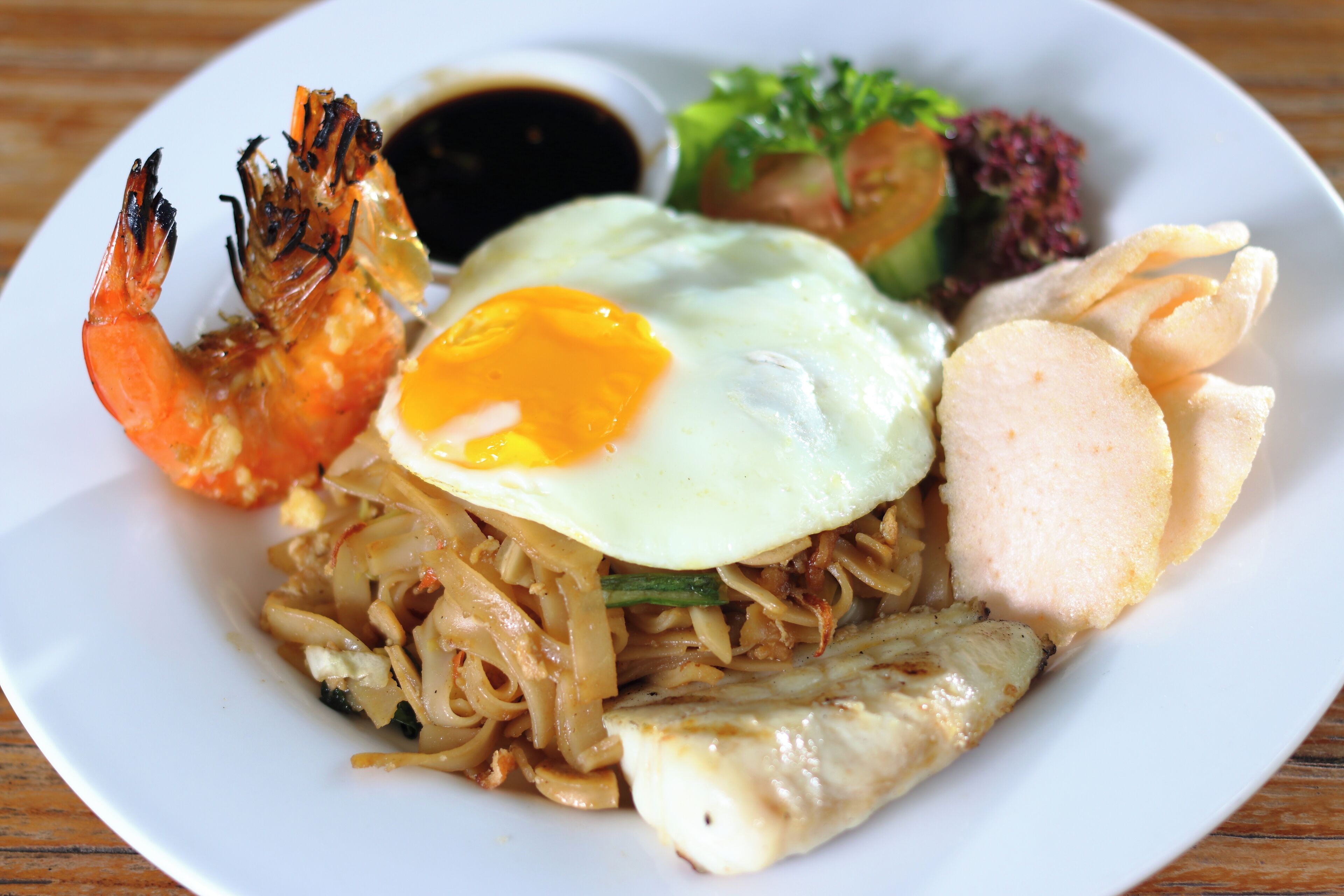 A plate of food with noodles, a fried egg, shrimp, and vegetables.