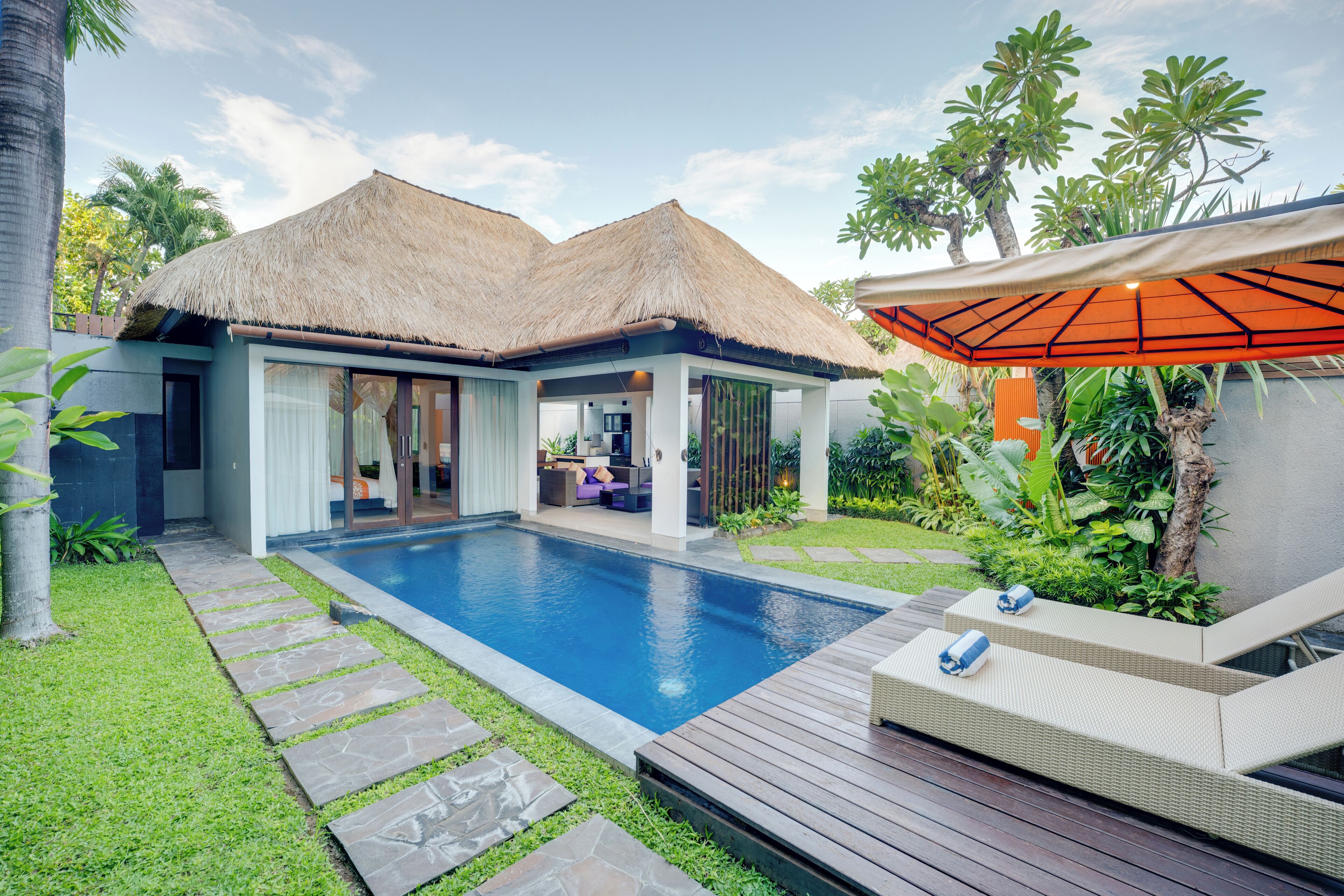 A modern villa with a swimming pool, outdoor seating, and lush greenery.